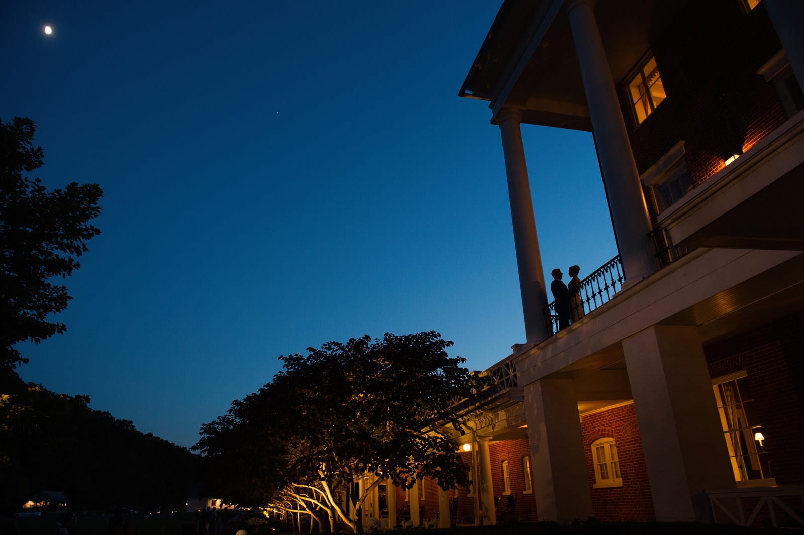 A bride and groom are silhouetted against the deep blue twilight sky as they stand on a balcony during their wedding at the Omni Bedford Springs resort.