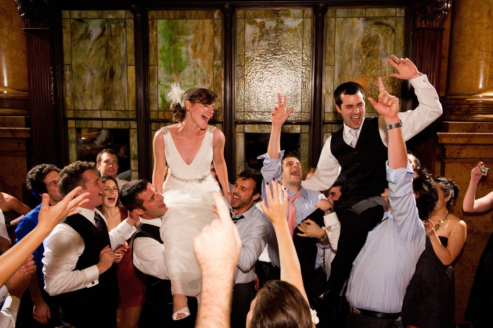 A bride and groom laugh as they are held aloft by their wedding guests at The Grand Concourse.