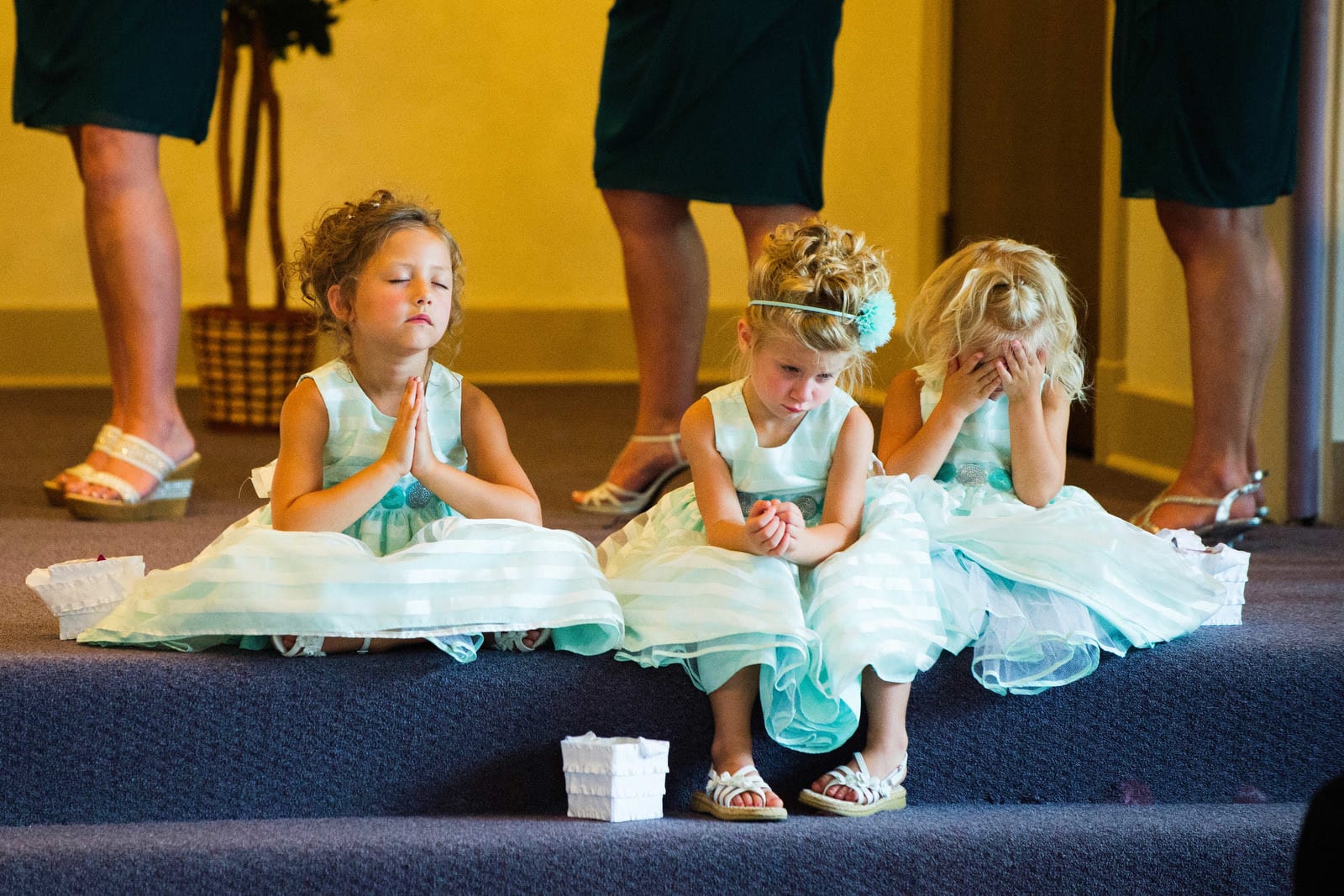 Three flower girls have very different reactions as they sit on the altar during a wedding.
