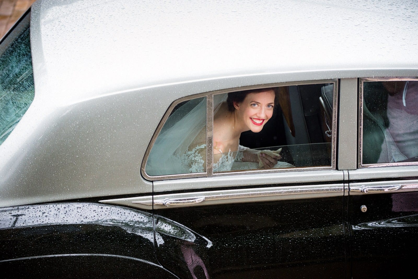 A bride smiles as she looks out of the window of a vintage Rolls Royce limousine before her wedding at the Omni William Penn hotel.