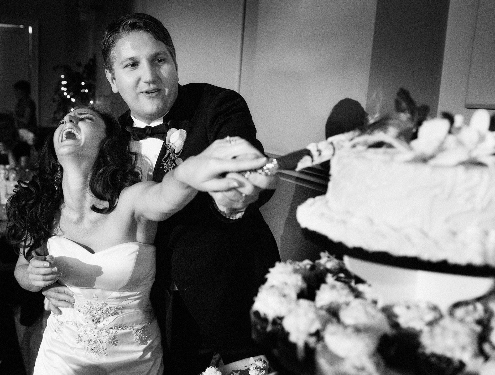 A bride laughs as she and her husband reach out to cut their cake during their wedding at Pittsburgh's Grand Hall.