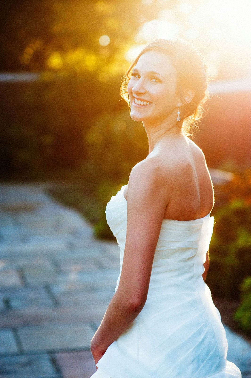 A bride looks over her shoulder and smiles at sunset after her wedding at the Pittsburgh Center for the Arts.