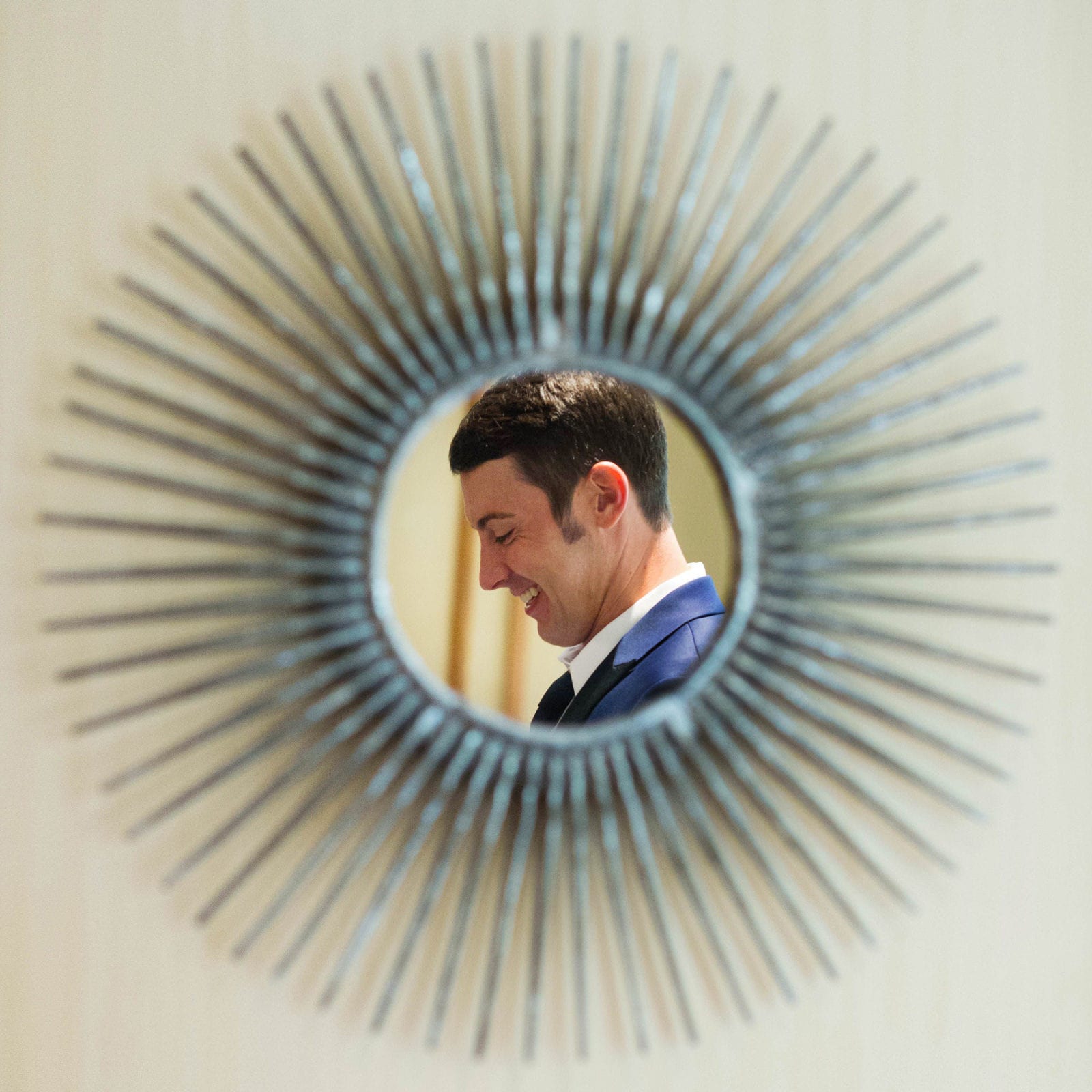 A smiling groom is reflected in a mirror with sunburst frame before a wedding at the Sheraton Station Square.