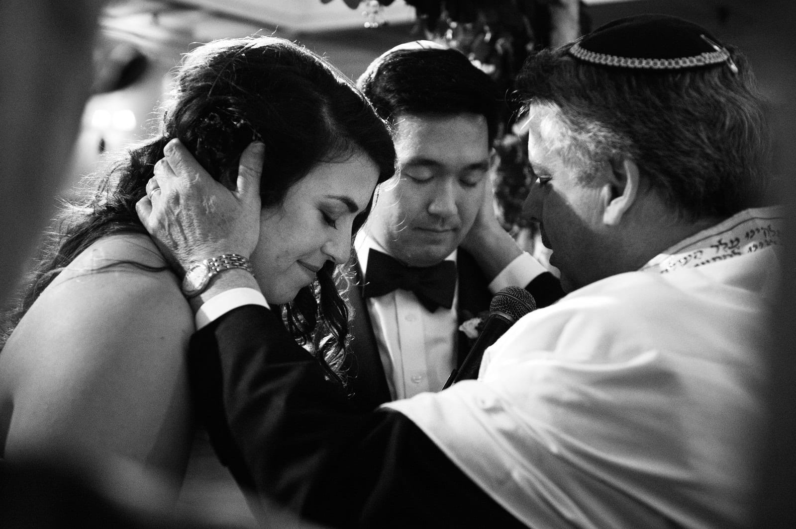 A rabbi holds the heads of a bride and groom as they pray with closed eyes during their wedding at the Pittsburgh Golf Club.