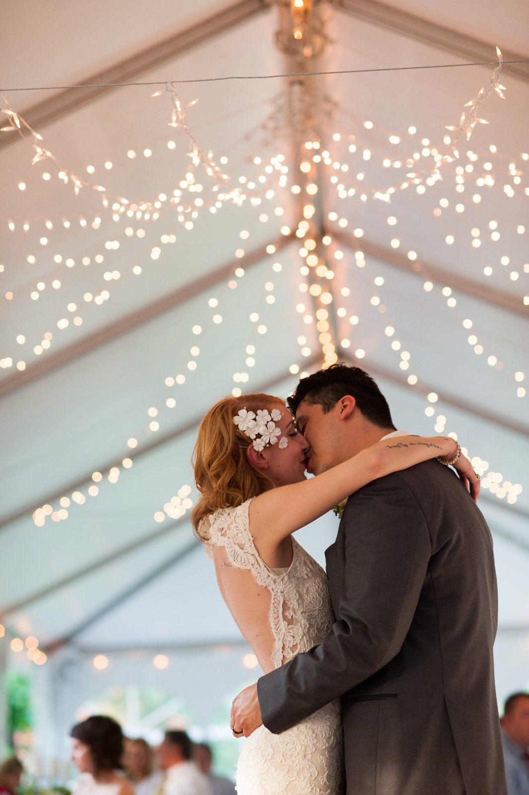 A bride and groom kiss beneath the twinkle lights in the tent outside of the Mansion at Maple Heights.