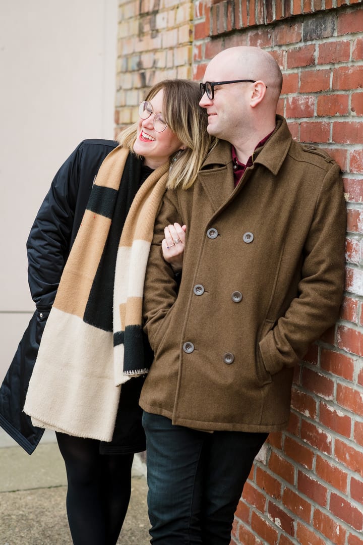 A couple leans against a brick wall during their winter engagement portraits in Pittsburgh.