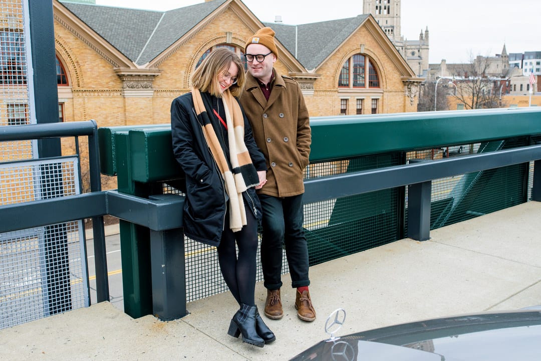 A couple leans against a green metal railing during their winter engagement portraits in Pittsburgh.