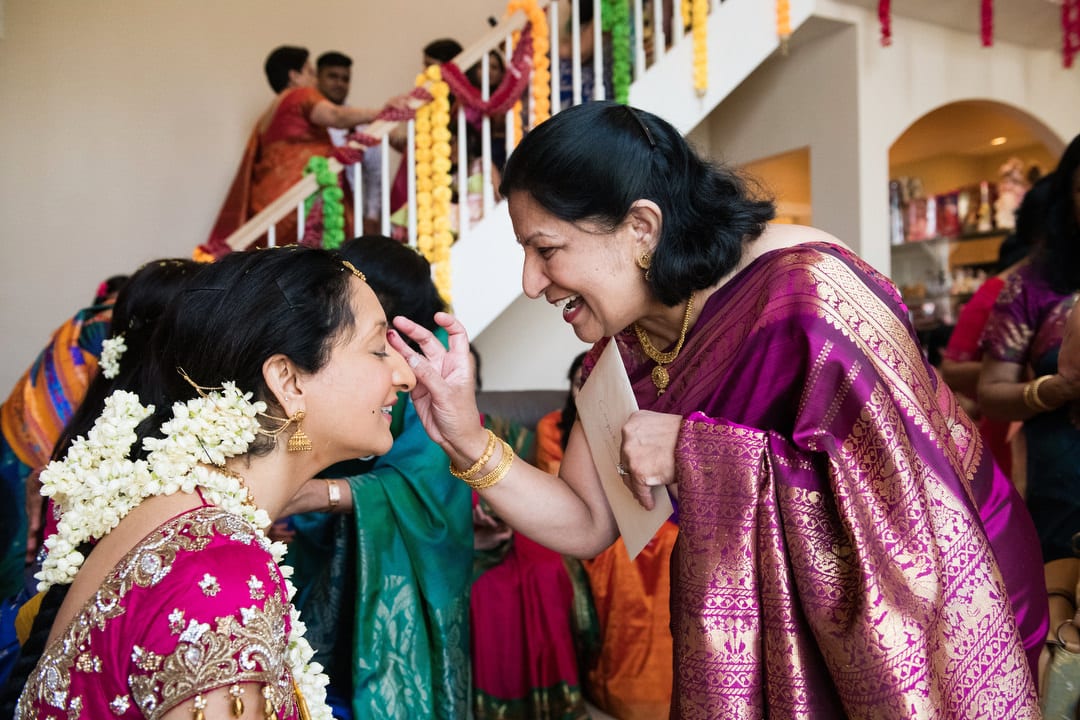 A woman wearing a sari applies a bindi to an Indian bride during a Puja.