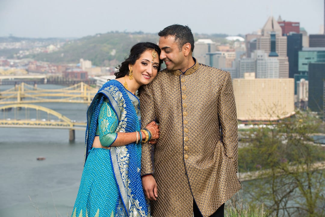A couple wearing blue and gold traditional Indian wedding garb stands high above downtown Pittsburgh before their Indian Wedding Pittsburgh Wyndham.