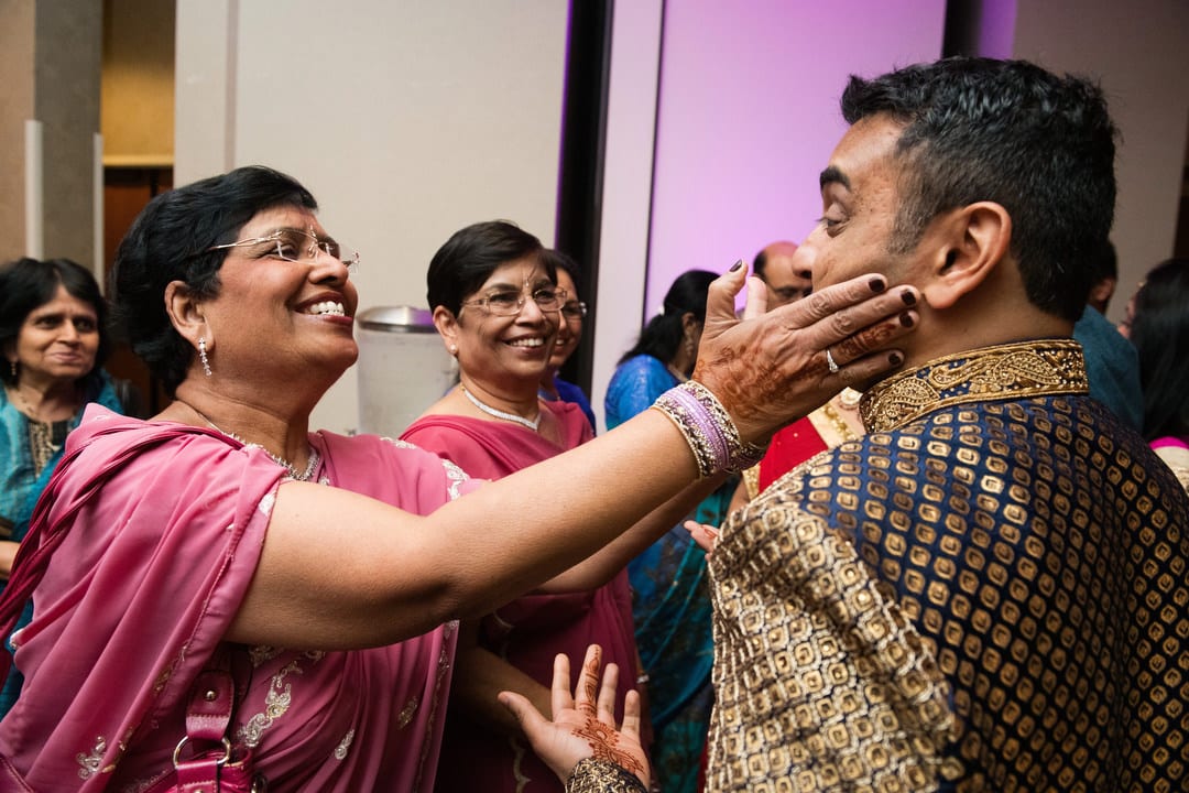 An Indian woman smiles and touches the cheek of a groom prior to his Sangeet.