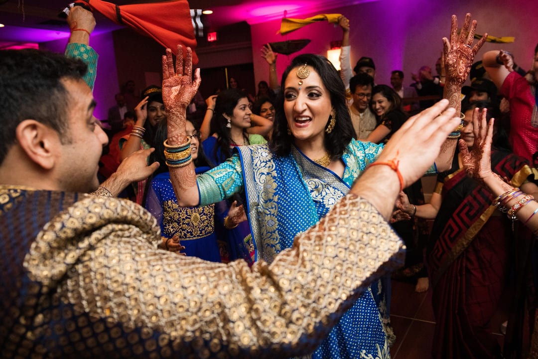 A bride and groom wearing traditional Indian wedding clothes dance with their guests during the Sangeet at the Wyndham Grand Pittsburgh.