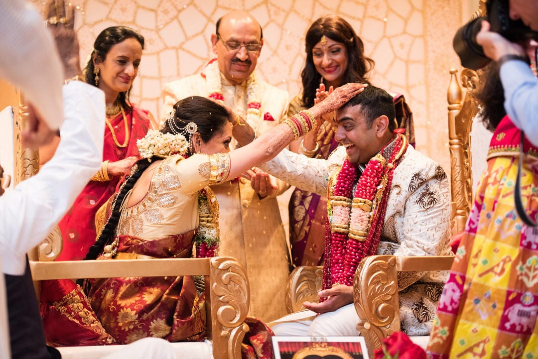 A bride and groom hold their hands on each other's heads as family members gather around during their Indian Wedding Pittsburgh Wyndham.