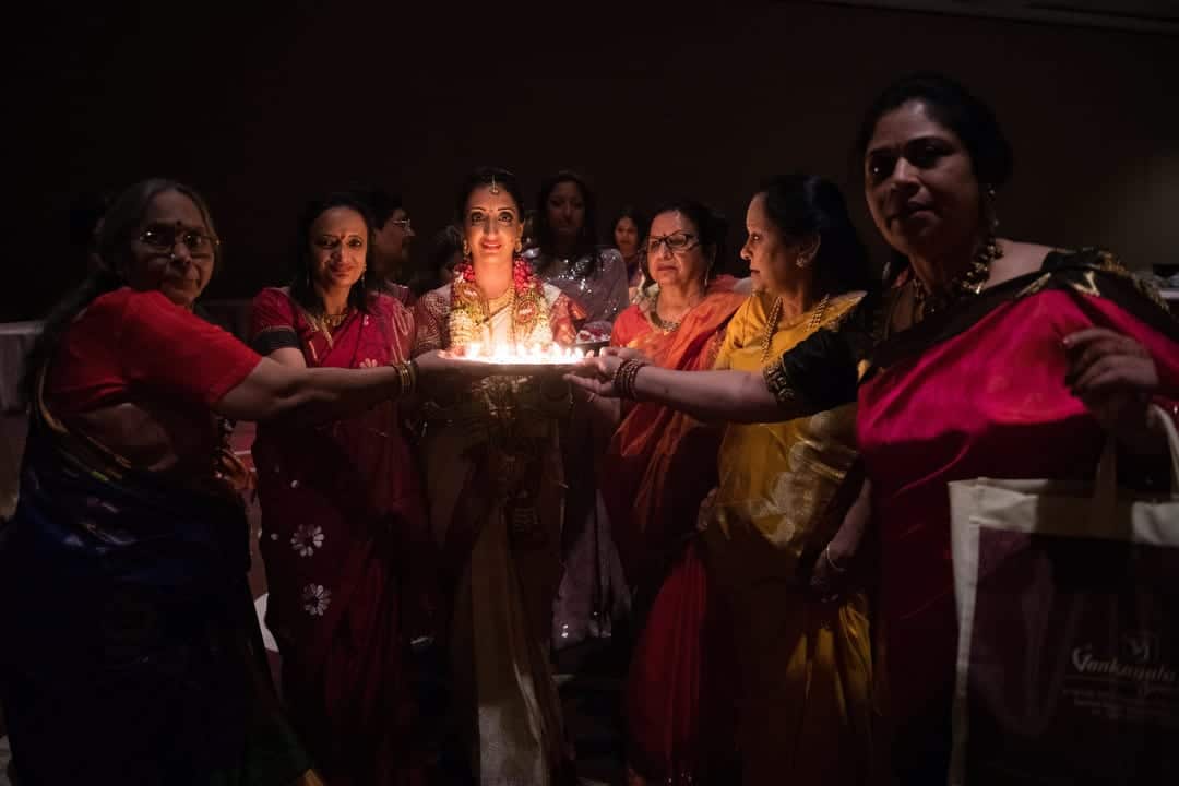 A bride wearing traditional Indian wedding clothing is illuminated by candles on a tray that she is holding.