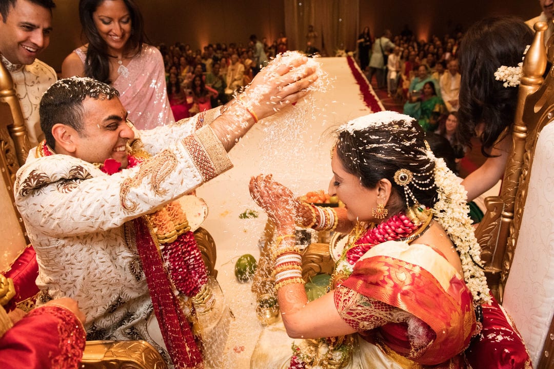 A bride and groom dump handfuls of rice over each other's heads during a traditional Indian wedding ceremony.