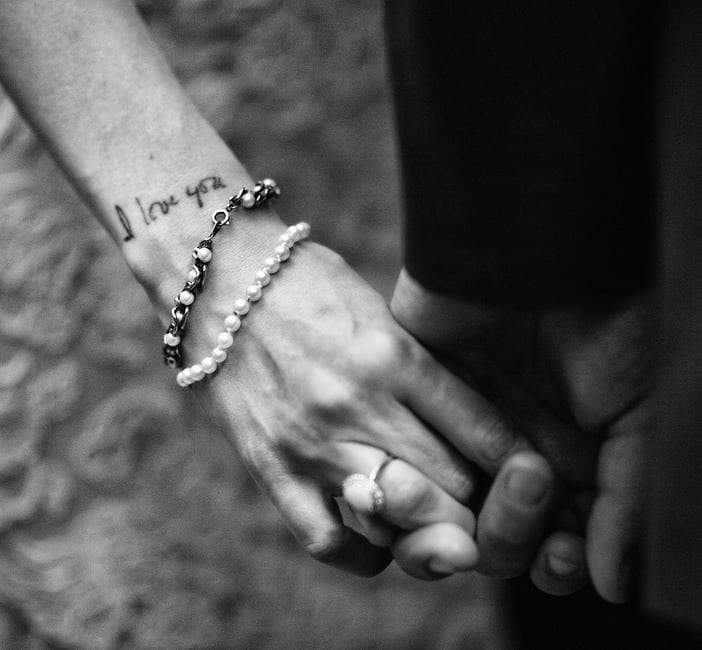 Detail photo of a bride and groom's held hands with the words "I love you" tattooed on the bride's wrist.