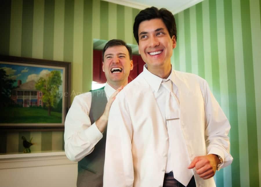 a groom and his best man laugh as they get dressed before a wedding