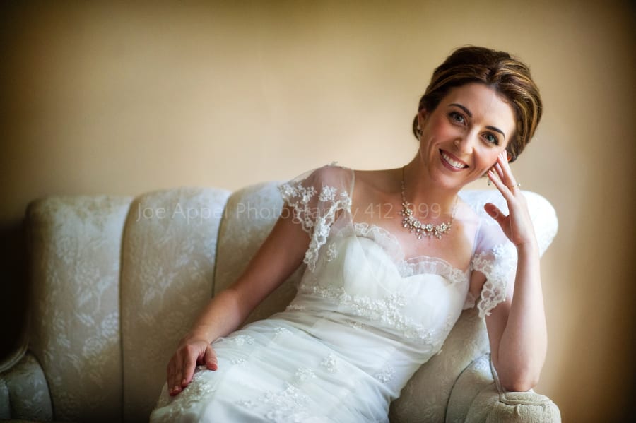 a beautiful bride reclines on a sofa softly lit by sunshine coming through a window