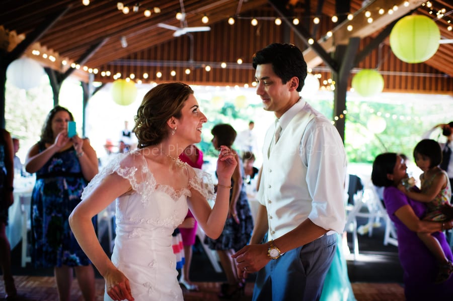 bride and groom dance together beneath the roof of an outdoor pavilion where they summertime wedding reception was held