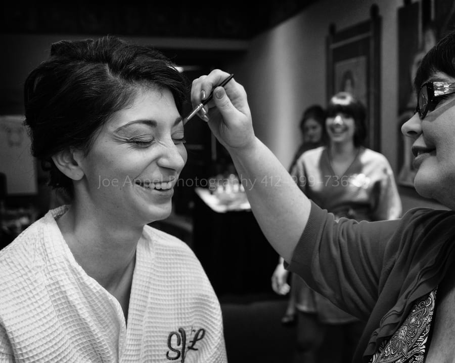 bride smiles as a makeup artist applies mascara to her West Virginia Wedding Photography