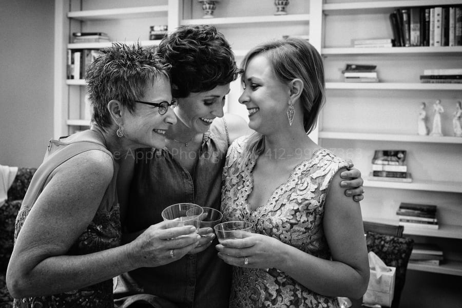A bride embraces her sister and mother as they drink a toast.