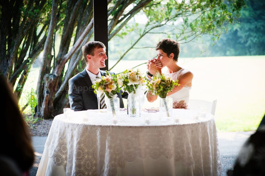 A bride kisses her husband's hand as they sit at their table during their wedding reception.