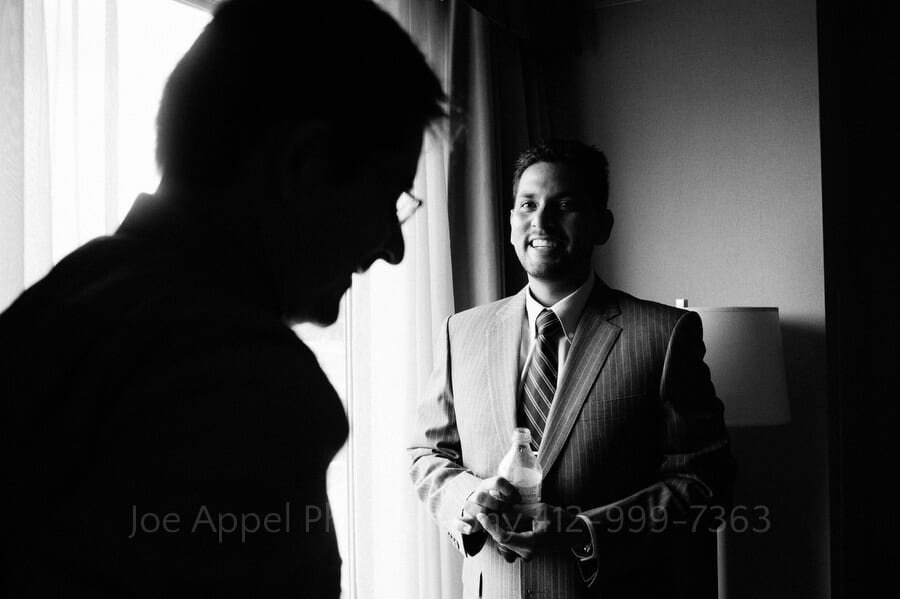 A groom smiles as he talks to a friend in a hotel room outdoor wedding in pittsburgh