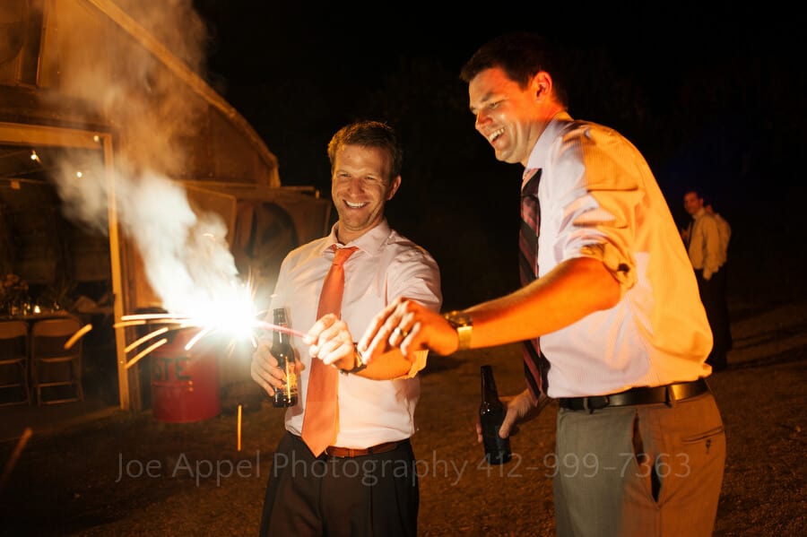 two men light sparklers in the dark during a wedding reception outdoor wedding in pittsburgh