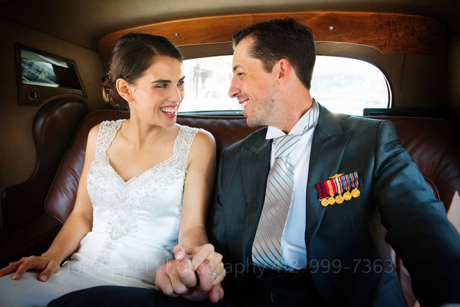 bride and groom hold hands and look at each other as they sit in the back seat of an antique Bentley