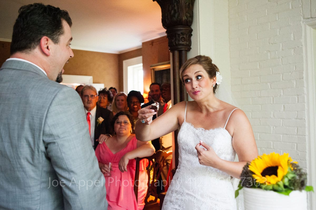 Bride makes a funny face at her groom as she holds a piece of cake out to her groom.