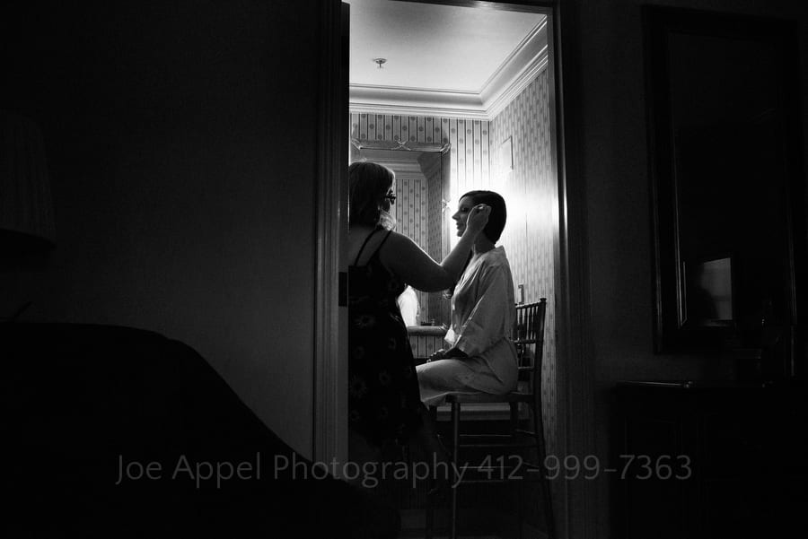 A woman is seen through an open doorway to a bathroom as she has her makeup applied before her wedding.