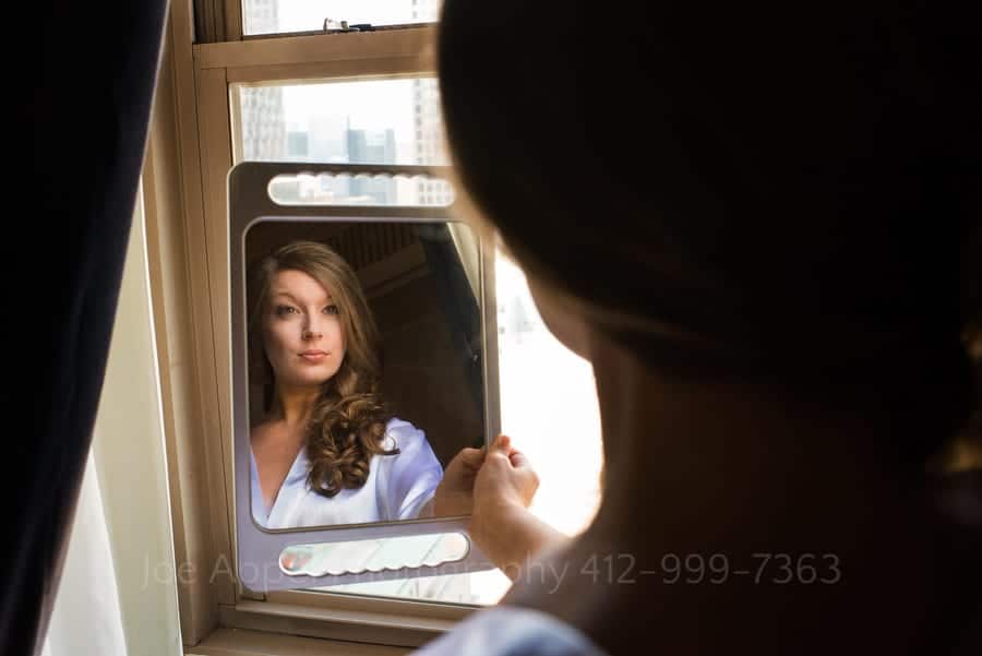 A woman holds a hand mirror checks her makeup in the window of a hotel suite at the William Penn Hotel in downtown Pittsburgh.