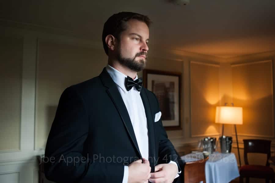 A groom buttons the jacket of his tuxedo while standing in his room at the Omni William Penn in Pittsburgh.