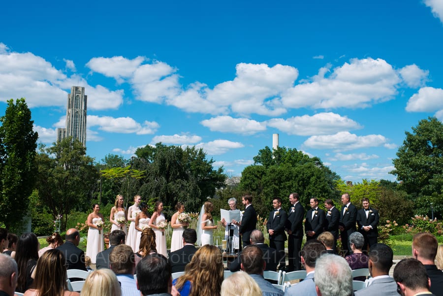 Puffy white clouds and the Cathedral of Learning form the backdrop for an outdoor wedding at Phipps Conservatory.