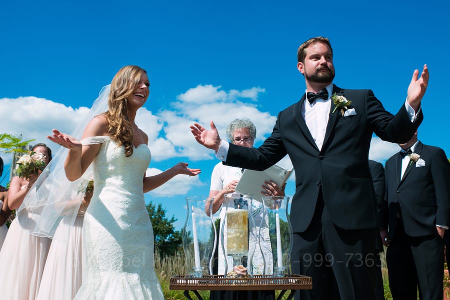 A bride and groom gesture with triumph after lighting their unity candle.