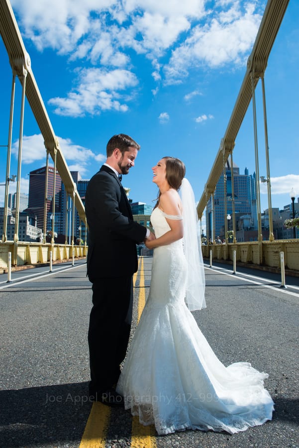 A bride and groom look at each other as they stand in the middle of the Roberto Clemente bridge in downtown Pittsburgh.