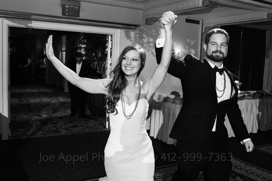 Bride and groom hold their hands up triumphantly as they enter their wedding reception in the grand ballroom at the Omni William Penn wedding.