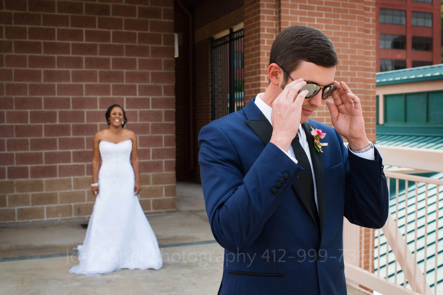 Groom removes his mirrored sunglasses as his smiling bride waits behind him to walk up for their first look before their Grand Concourse Wedding.