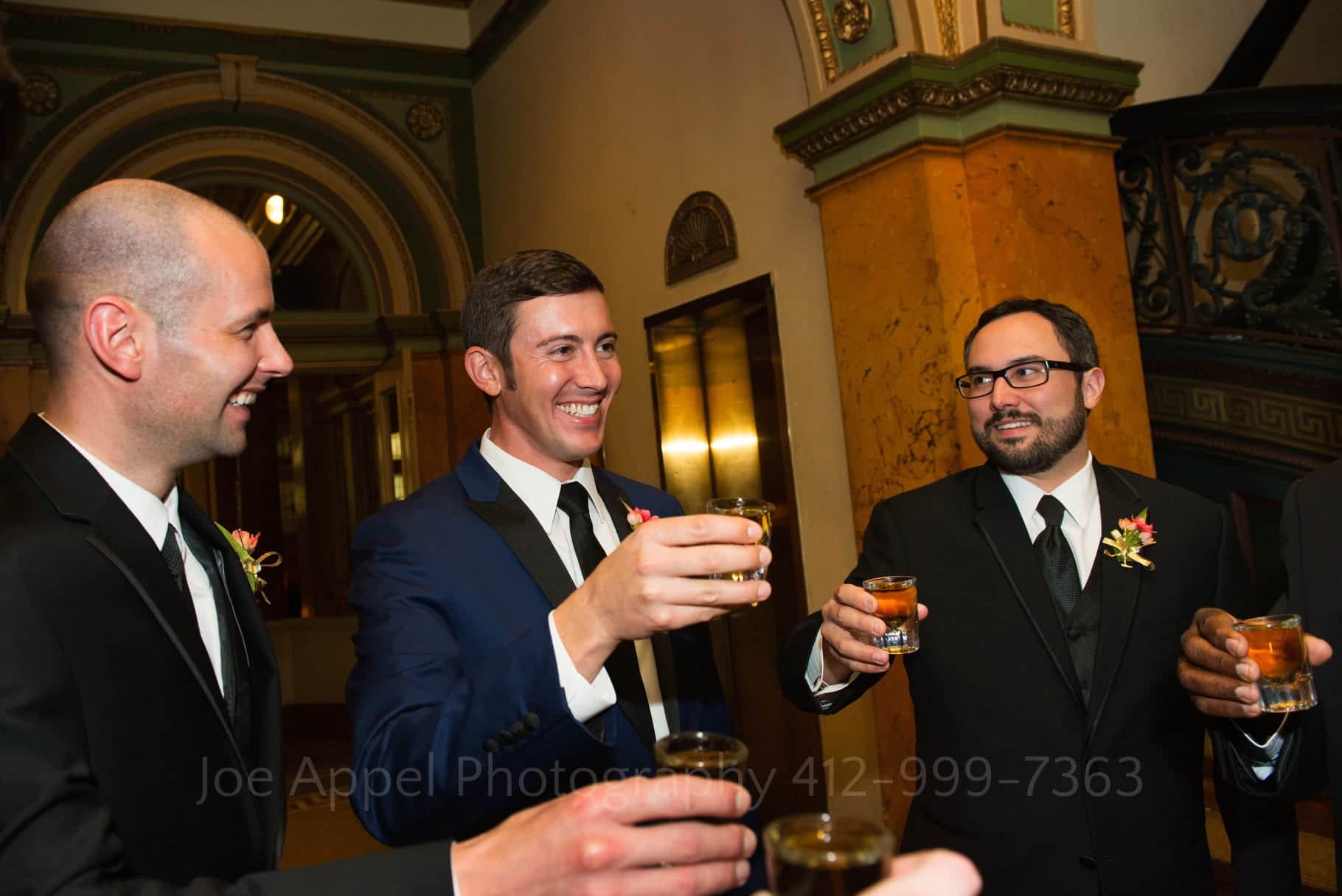Groom and his groomsmen hold glasses of whiskey as they toast prior to his Grand Concourse Wedding.