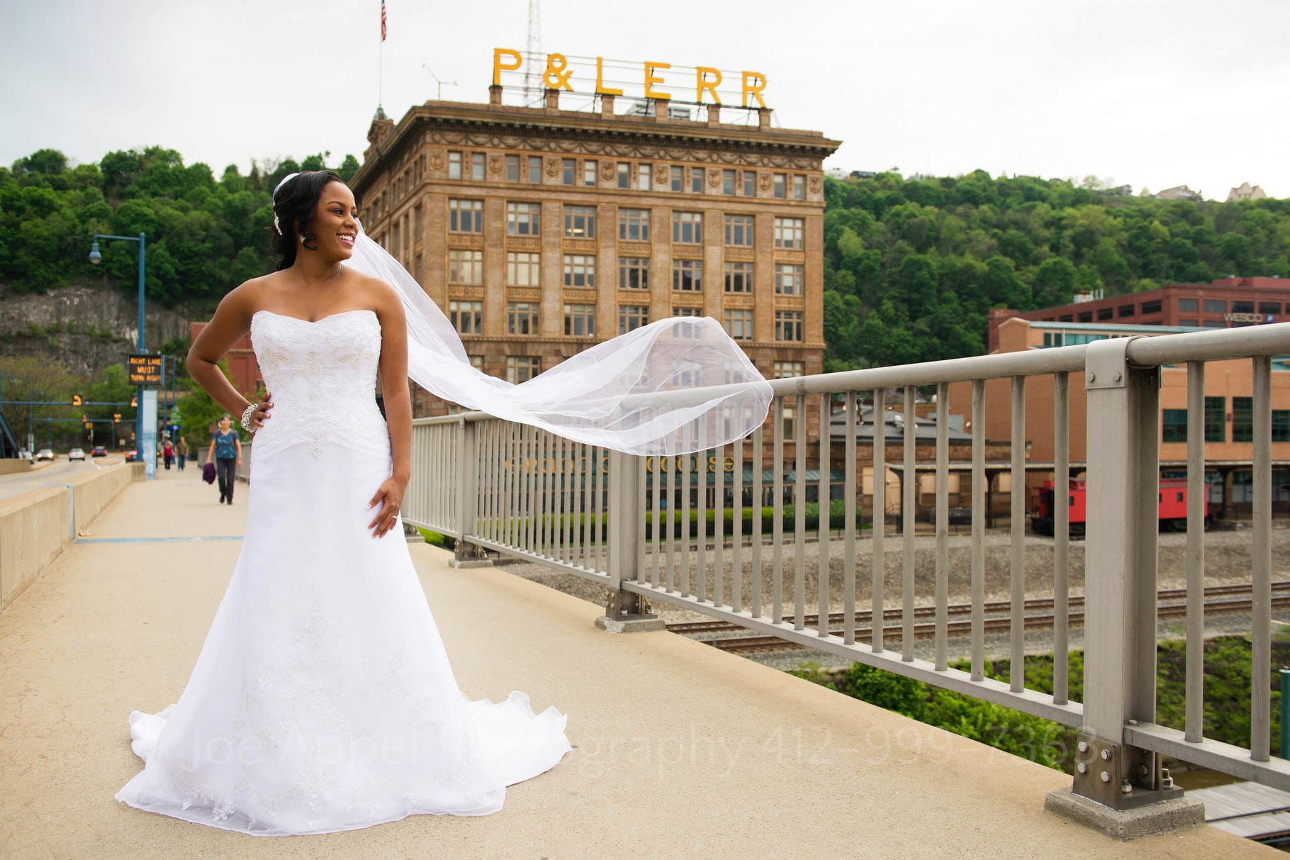 A bride looks to the right as her veil blows in the wind with the Pittsburgh and Lake Erie Railroad behind her.