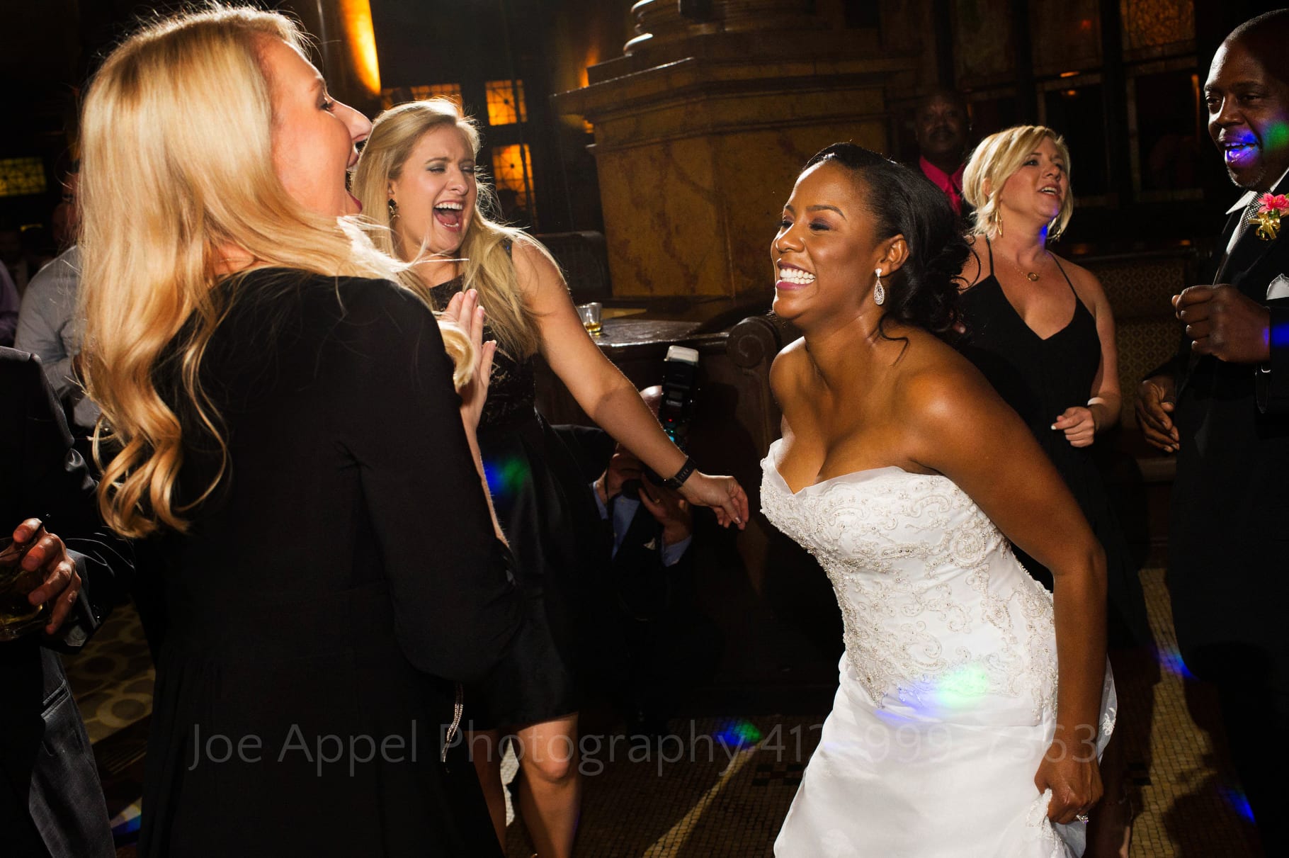 A bride faces left while dancing with three blond friends wearing black dresses.