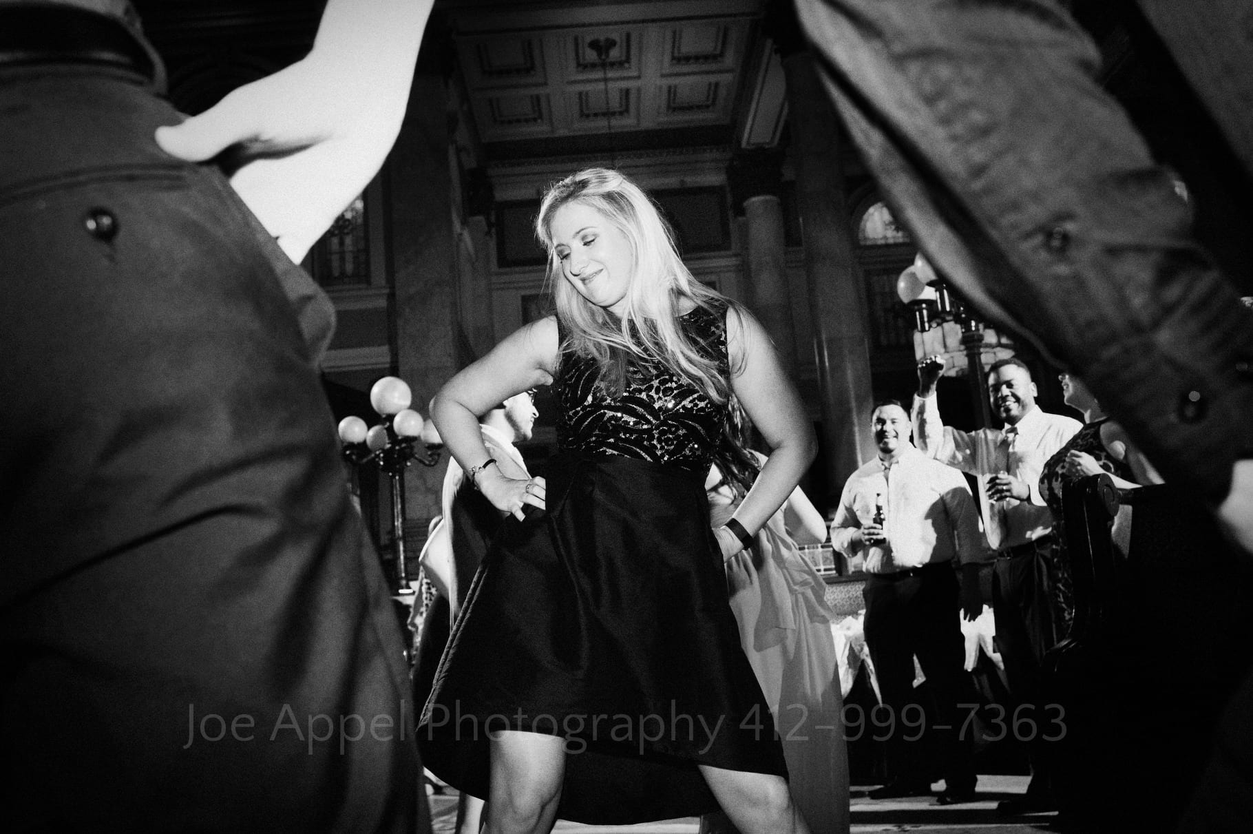 Framed by other guests, a woman dances with her hands on her hips during a Grand Concourse Wedding reception.