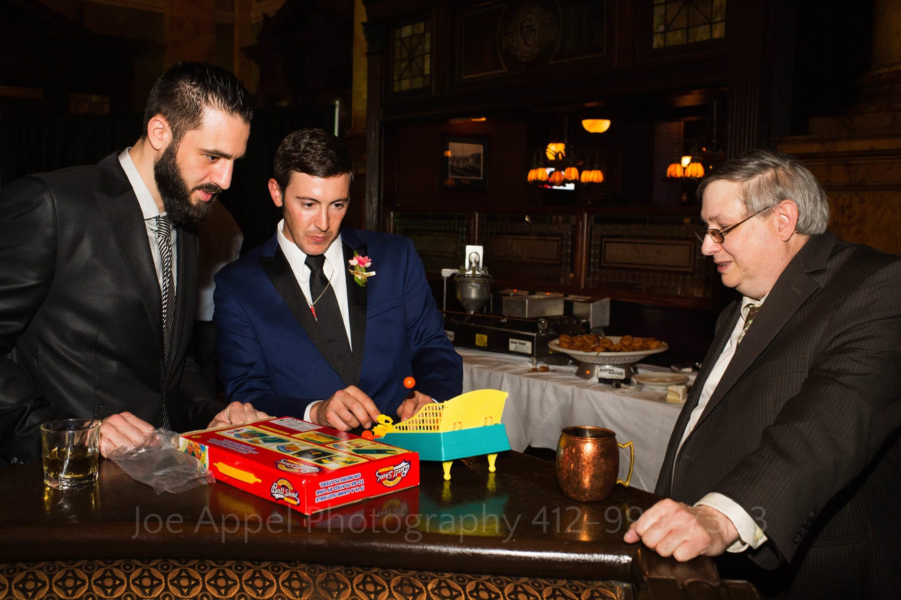 Groom plays a table top basketball game called Ball Shoot with guests during his wedding reception. Behind him is the donut making robot at the Grand Concourse.
