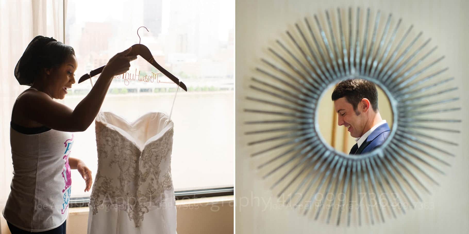 A bride smiles as she holds her wedding dress by a personalized hanger in front of a hotel room wedding. A groom is reflected in a mirror shaped like a sunburst.