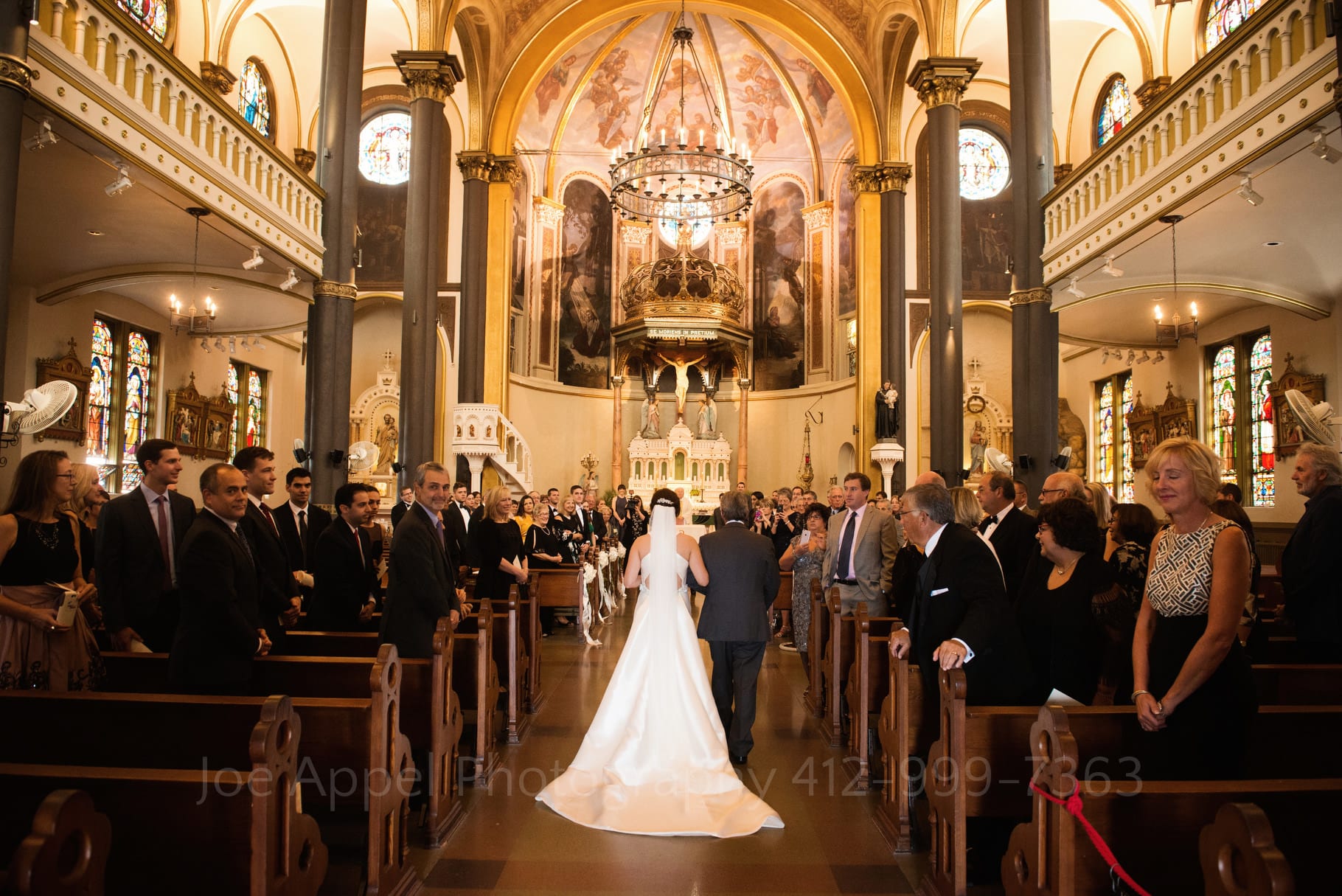 Viewed from behind, a bride and her father walk down the aisle at St. Stanislaus church.