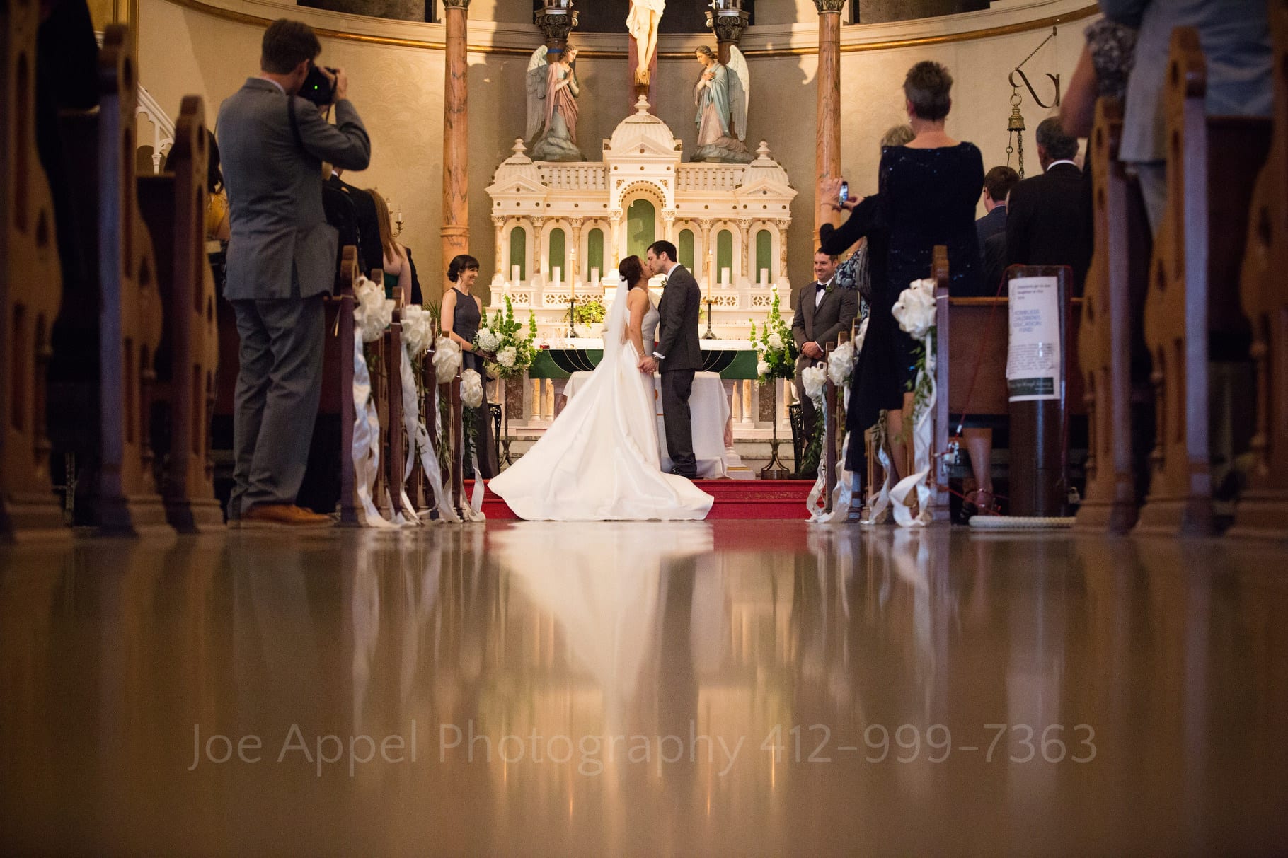 A bride and groom are reflected in the floor of St. Stanislaus church as they kiss in front of the altar during their wedding.