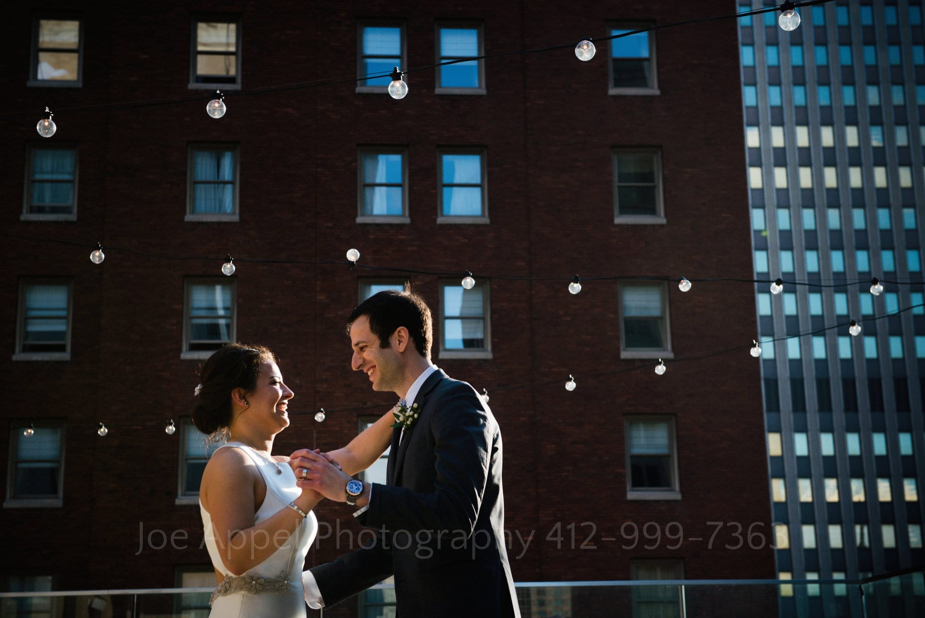 A bride and groom are rimmed in sunlight as they practice their first dance on the roof of the Hotel Monaco.