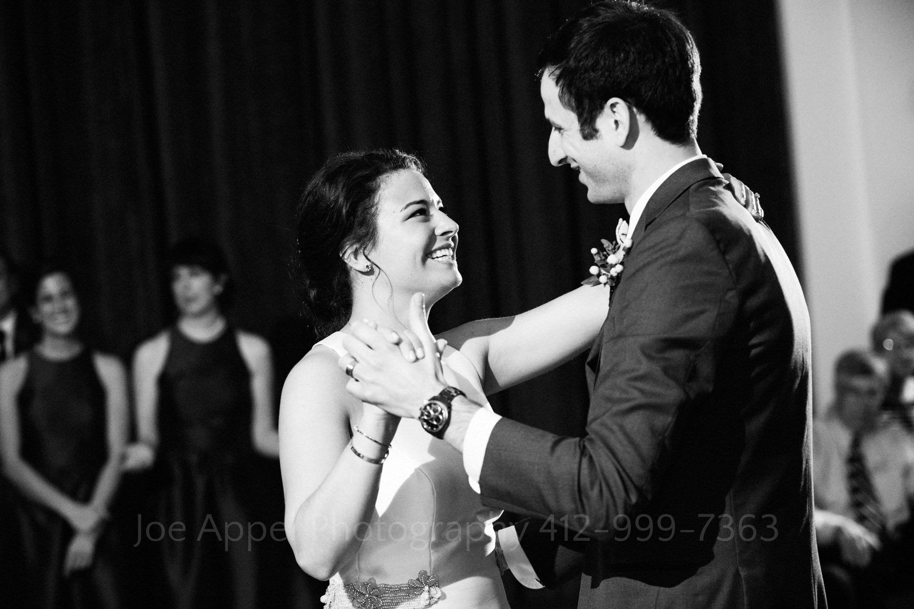 A bride and groom smile at each other as they enjoy their first dance at their Hotel Monaco Wedding.