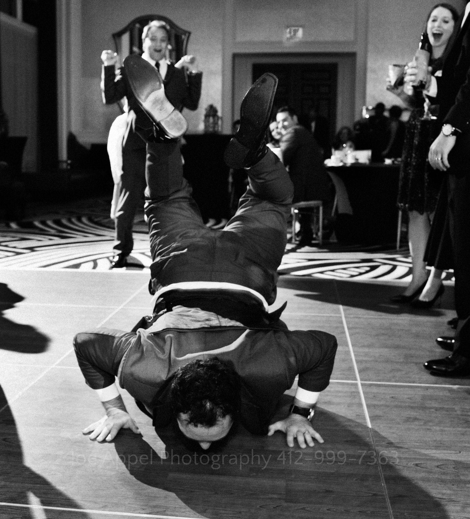 A man has his hands and face on the ground as his feet are up in the air while other guests look on and laugh at the Hotel Monaco.