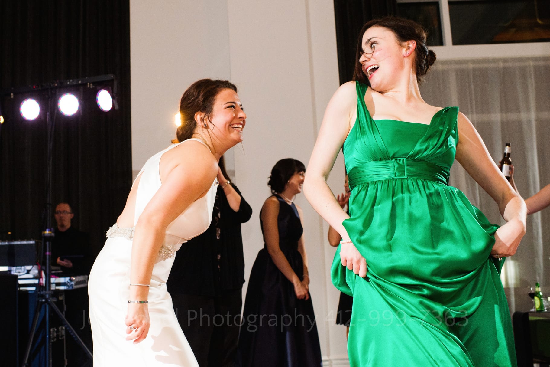 A woman in a green satin dress dances with a bride in a white dress at her Hotel Monaco wedding.