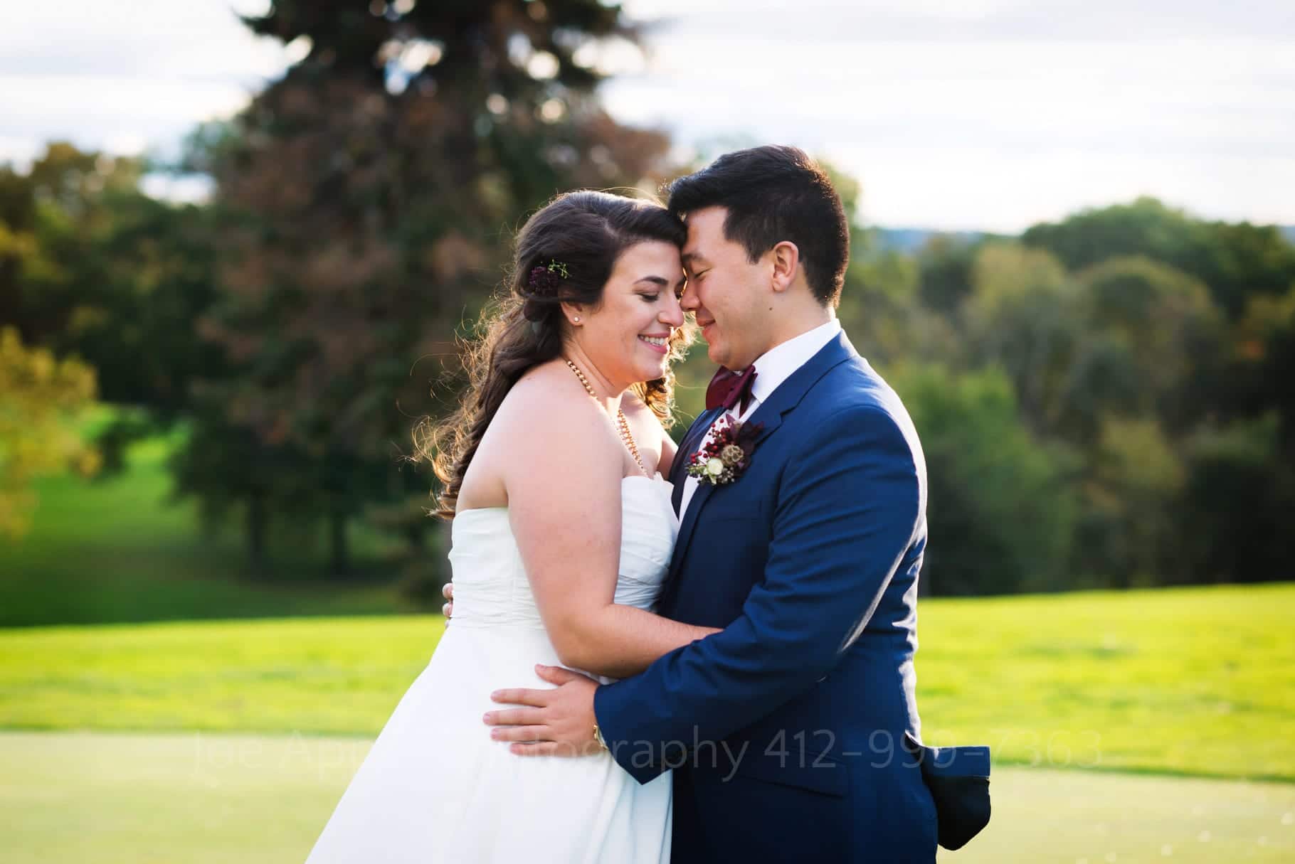 A bride and groom touch foreheads as they embrace while standing on a golf course.